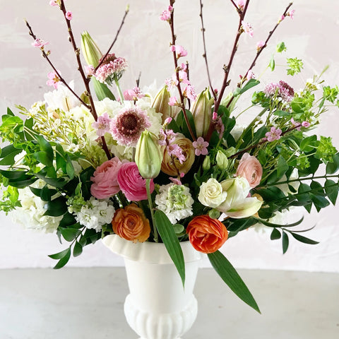 Floral arrangement with pink, white, and orange flowers in a white vase on a light background
